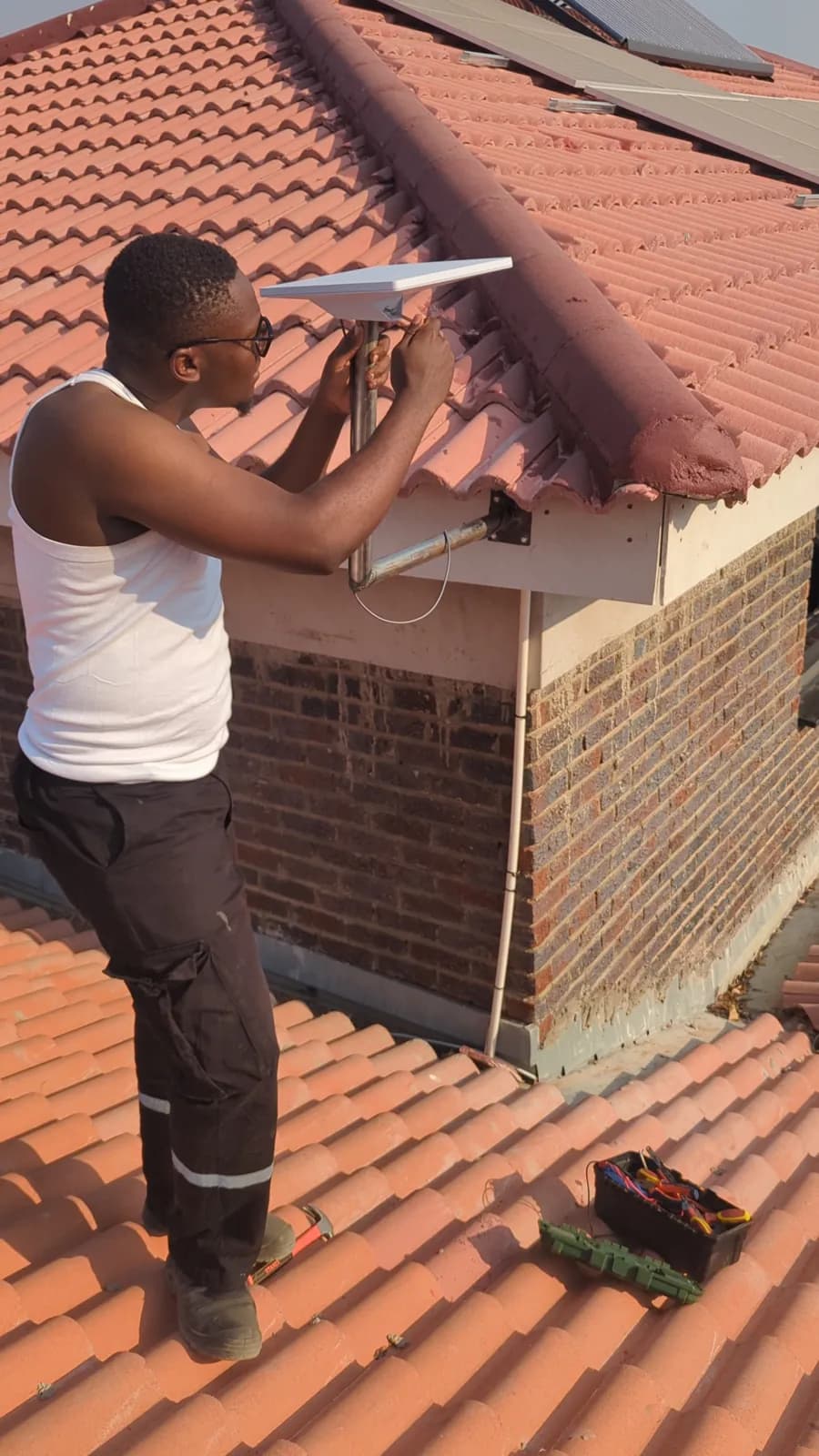 Starlink: A technician fixing the dish to its mast at the gable, above the roof tiles in Goromonzi, Zimbabwe