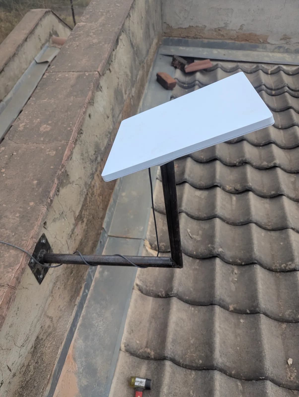 Starlink dish on a wall bracket beside a tiled roof in Zimbabwe